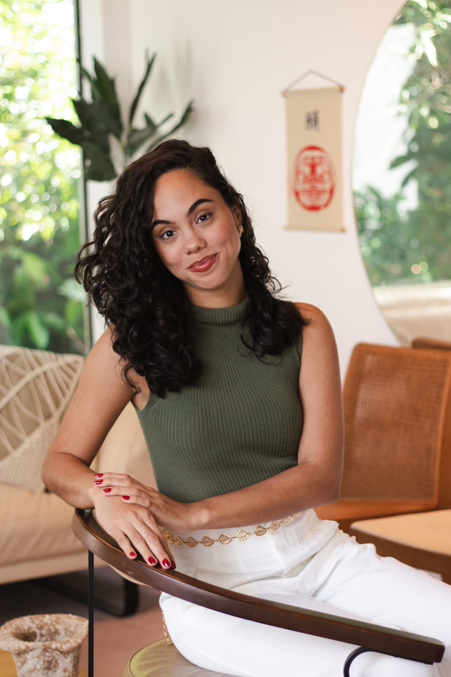Retrato de Lorena Ribeiro, sorrindo, de blusa verde, sentada em uma poltrona